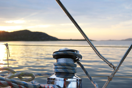 Skeleton winch on board a sailing cruise yacht. The view from the cockpit on the sunset background....