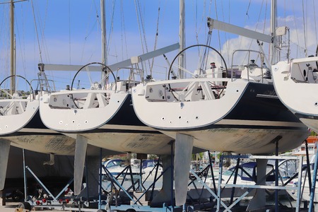 Same yachts stand in a row on the dry parking in the marina on a sunny summer day. Device sailing...