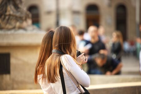Young long-haired brown-haired girls walk in the center of the ancient city. Fashion of modern youth. Free time and happy weekend. Blurred background. Ancient architecture and design of buildings.の写真素材