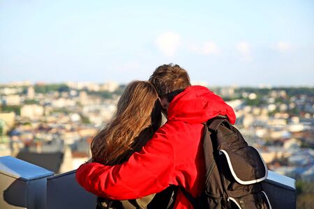 A guy in a red jacket is standing in an embrace with a long-haired girl. A young couple at the observation deck of the Lviv City Hall peers into the panorama of the ancient city. Couple in loveの写真素材
