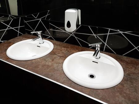 Bathroom interior in black and white. Round ceramic washbasins. Mirrors, plastic soap dish and chrome faucets for washing hands after a toilet. Design with dark facing tiles.の写真素材
