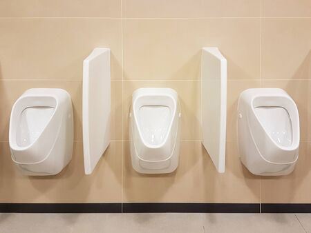 Bathroom interior in light beige and white colors. Oval ceramic urinal. Place of need for men. Restroom in public areas of urban infrastructure. Interior of public spaces.の写真素材