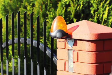 Orange room alarm light located on a brick fence post. Intercom apartment building at the entrance to a private protected area. Hazard alert. Intercom for door curtain. Property Protection and Securit.の写真素材