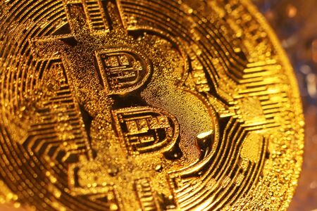 A bitcoin gold coin frozen in ice covered with drops of moisture iridescent in the rays of light....