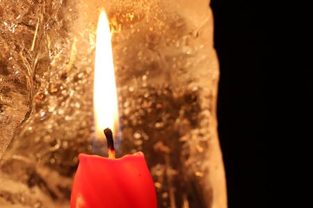 Christmas and New Year decoration. Burning red candle with ice on a dark background. Happy mood on a family holiday. Artistic design for the winter holidays. Warm light.の写真素材