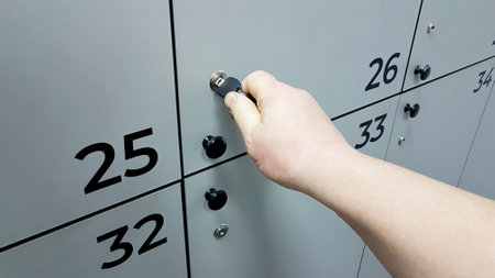 A man's hand opens the door of a locker for storing personal items in a public locker room with a key. Furniture for a sports complex or enterprise. Thirso-plate productの写真素材