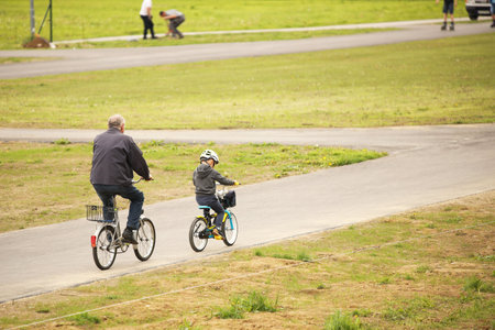 Grandfather and grandson ride bicycles on the asphalt path of the park. Raising the younger...