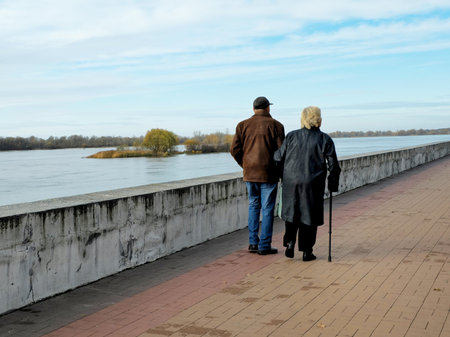 An elderly couple walk hand in hand along the embankment in the autumn season. Romantic relationships in old age. Old age is not an obstacle to family relationships of love and respectの写真素材