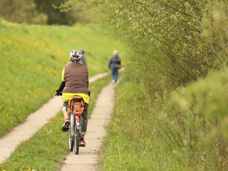 An old gray-haired woman rides a bicycle among the greens. A healthy and active part of life. Ecological transport for the population. Free time for retirement. Movement in space. Sports for the elders.の写真素材