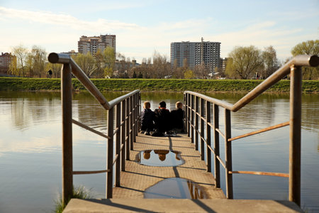 Three boys and friends are sitting on a bridge with metal handrails over the water. Friendly conversation in nature. Children's play outdoorsの写真素材