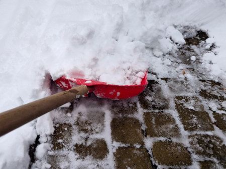 Clearing snow from the sidewalk with a red plastic shovel in winter. Cleaning snow-covered areas.の写真素材