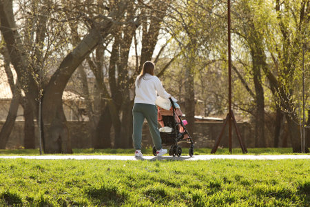 A young mother walks in the park with a baby carriage on a sunny day. Baby's stay in the fresh air.の写真素材