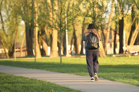 A young girl walks alone along a park alley. A walk in the fresh air among summer greenery. Fashion of modern youth.の写真素材