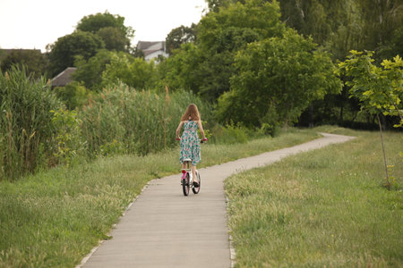 A girl rides a bicycle on an asphalt avenue among the greenery of the park. Active fun outdoors. Sports load for the proper development of the girl's body.の写真素材
