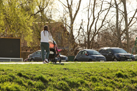 A young mother walks in the park with a baby carriage on a sunny day. Baby's stay in the fresh air.の写真素材