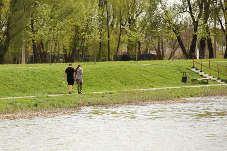 A man and a woman are walking in the park along the lake shore. A walk of lovers in the fresh air on a day off. Family leisure in natureの写真素材