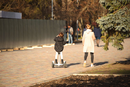 A young mother and daughter walk along the promenade. A girl riding a park on a gyro scooter. Modern...