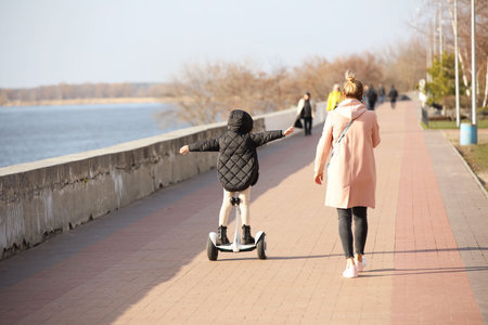 A young mother and daughter walk along the promenade. A girl riding a park on a gyro scooter. Modern...