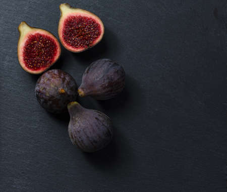 Still life of black figs. Three whole figs and one split fig. Dark Food.