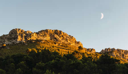 Sunset on mountain peak with waning moon.