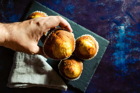 Hand picking up a muffin from the slate plate with linen cloth on a rusty blue background. Dark...