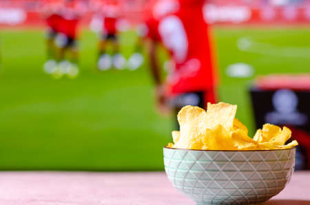 Bowl of potato chips to watch soccer. Snack with out of focus sports background.