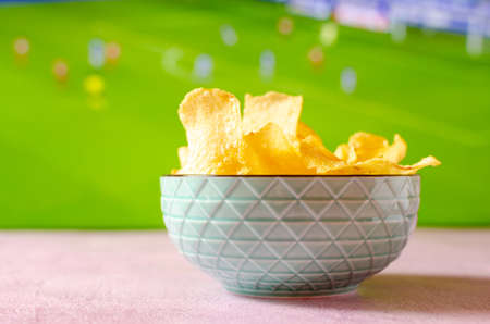 Bowl of potato chips to watch soccer. Snack with out of focus sports background.の写真素材