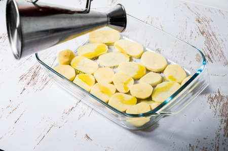Unrecognizable person adding oil to a bed of potatoes in a glass baking dish to prepare a chicken cava in the oven.の写真素材