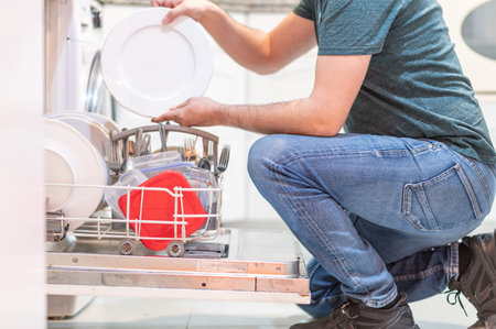 Unrecognizable adult male setting the dishwasher. Man doing housework. Concept of feminist equalityの写真素材