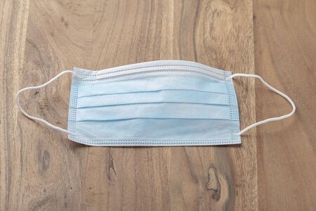 Photo of a blue surgical mask placed on a wooden table made of solid brown oak. The mask with its...