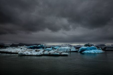 Several glaciers floating in the Jökulsárlón, a glacier lagoon in the south-east of Iceland. They are numerous and have light blue, azure, and white reflections. The sky is gray.の写真素材