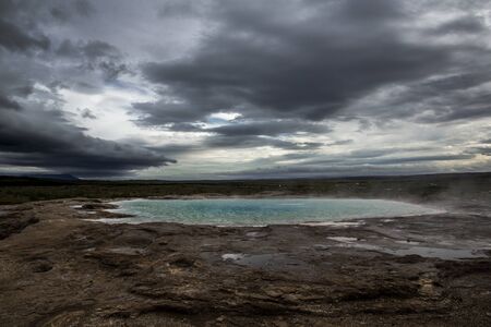 hot spring at the Geysir site in central Iceland. The water is heated by geothermal energy and gives off a slight egg-like smell from the sulfur rising from the earthの写真素材