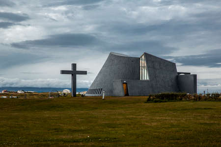 Landscape in Iceland. There is a church with modern architecture made of gray concrete. The sky is cloudy and the vegetation is brown and green.のeditorial素材