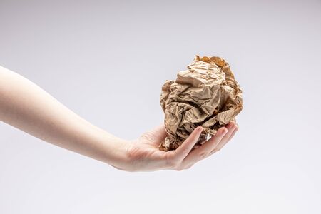 Close-up of a white people's hand holding a crumpled piece of brown paper in front of a white backgroundの写真素材