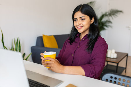Young indian woman sitting on table using laptop at homeの写真素材
