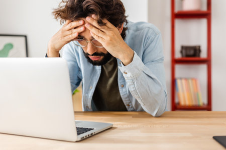 Exhausted young man receiving online bad news