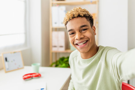 Smiling teenage boy taking selfie with smart phone in his room