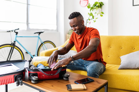 Young african man packing clothes to luggage before going on summer holidaysの写真素材