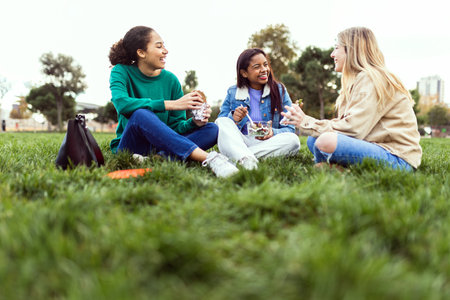 Three young female students having lunch sitting on grass at campus collegeの写真素材