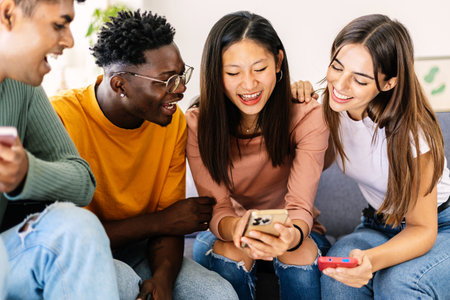 Young group of friends using mobile phone together sitting on sofa at home