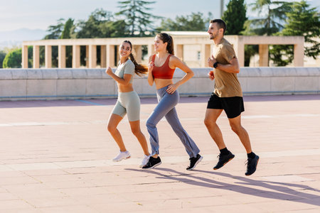 Three sportive young friends running together along an urban parkの写真素材