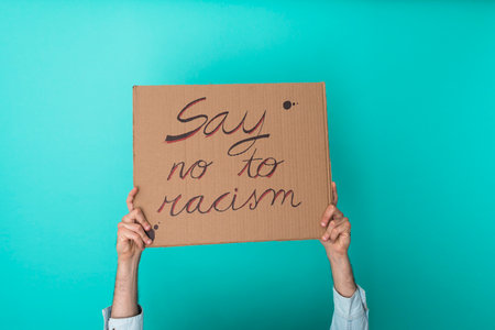 Crop anonymous person holding banner against racism over blue background - Equal rights conceptの写真素材