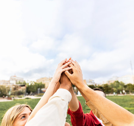 Diverse young adult people stacking hands showing unity outdoors.の写真素材