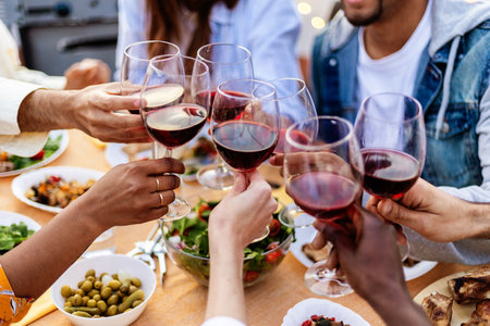 Close-up view of multiracial group of people toasting red wine at summer partyの写真素材