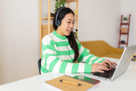 Young asian woman using headset looking at laptop screen while learning onlineの写真素材