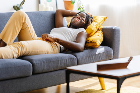 Young african woman relaxing on sofa smelling aromatic incense smoky stickの写真素材