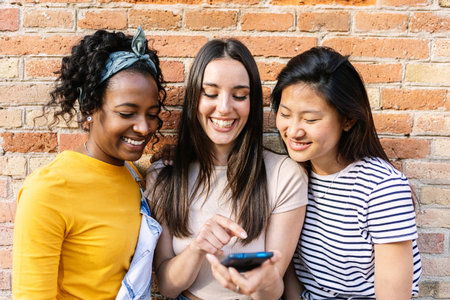 Happy young girls using mobile phone outdoorsの写真素材