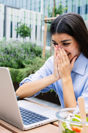Overjoyed businesswoman reading unexpected message on laptop computer outdoors.