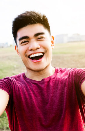 Happy asian young man taking a selfie portrait with mobile phone in city park