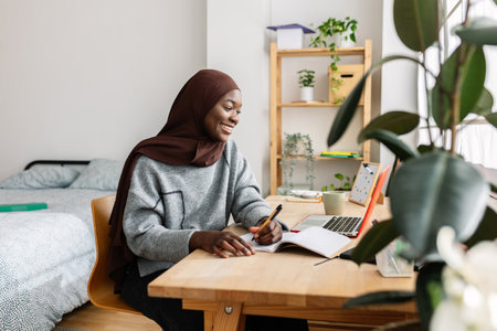 Happy young african millennial woman studying online using laptop at home.
